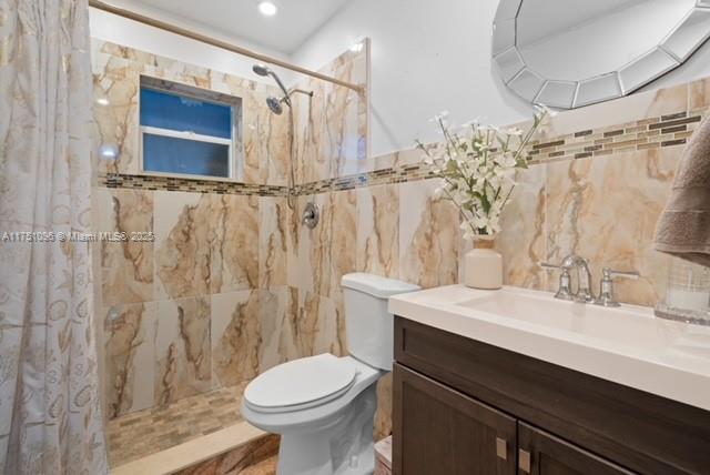 full bath with toilet, tile walls, a tile shower, and vanity