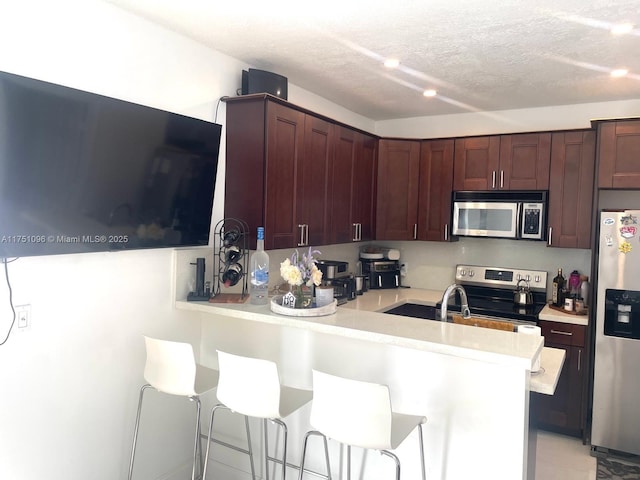 kitchen featuring a breakfast bar area, stainless steel appliances, light countertops, a textured ceiling, and a peninsula