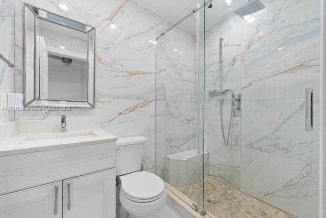bathroom featuring toilet, a marble finish shower, vanity, and tile walls