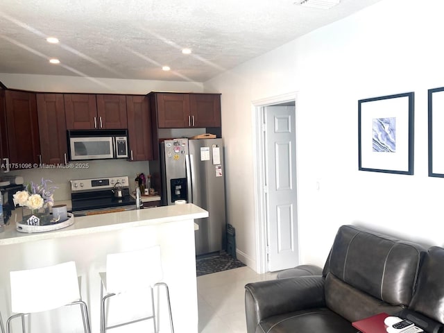 kitchen with a textured ceiling, a kitchen breakfast bar, open floor plan, light countertops, and appliances with stainless steel finishes