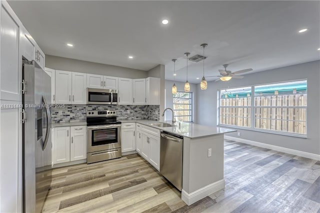 kitchen featuring visible vents, appliances with stainless steel finishes, decorative light fixtures, a peninsula, and a sink