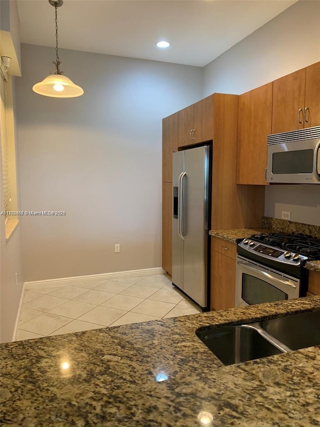 kitchen featuring light tile patterned floors, stainless steel appliances, hanging light fixtures, and brown cabinets