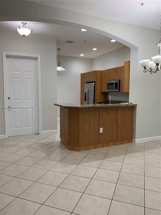 kitchen featuring light tile patterned floors, a peninsula, hanging light fixtures, appliances with stainless steel finishes, and brown cabinetry