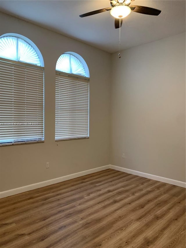 empty room with dark wood-type flooring, baseboards, and a ceiling fan