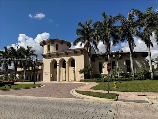 mediterranean / spanish home featuring a front yard, decorative driveway, a tiled roof, and stucco siding