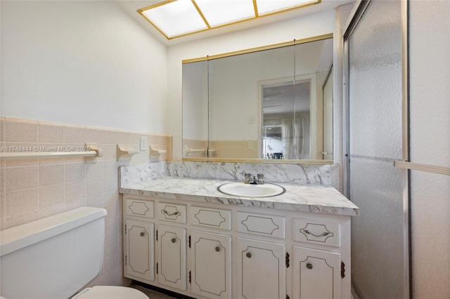 bathroom featuring toilet, a wainscoted wall, tile walls, and vanity