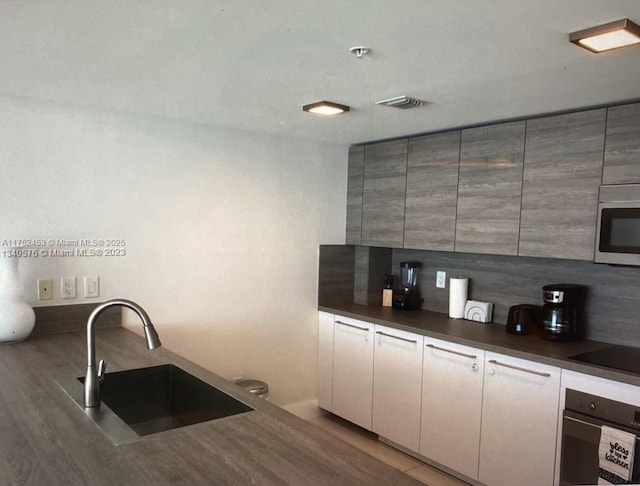 bar featuring black appliances, backsplash, and a sink