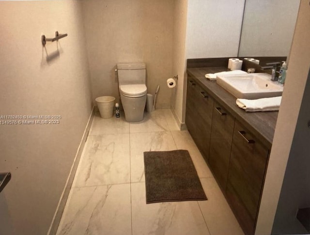 half bathroom with baseboards, vanity, and toilet