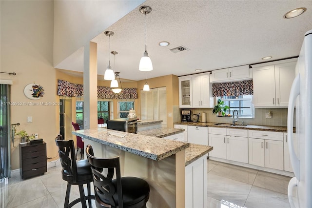 kitchen featuring a center island, backsplash, light tile patterned flooring, a sink, and white appliances