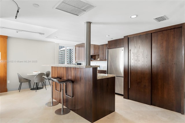 kitchen featuring dark brown cabinetry, visible vents, a kitchen island, a breakfast bar, and freestanding refrigerator