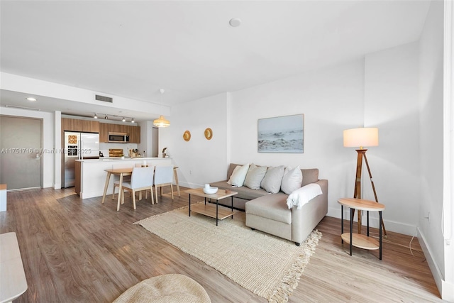 living area with rail lighting, visible vents, light wood-style flooring, and baseboards