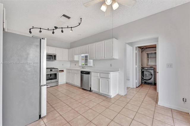 kitchen with appliances with stainless steel finishes, washer / clothes dryer, light countertops, and white cabinets