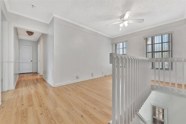 empty room with a textured ceiling, light wood-style flooring, a ceiling fan, baseboards, and crown molding