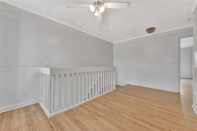 spare room with baseboards, ceiling fan, a textured ceiling, crown molding, and light wood-style floors