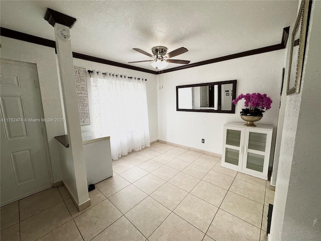 spare room with ceiling fan, a textured ceiling, crown molding, and light tile patterned flooring