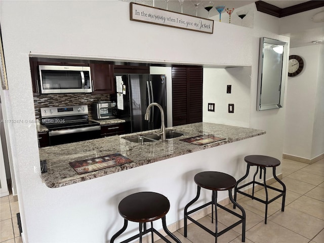 kitchen with appliances with stainless steel finishes, a sink, light stone counters, and a kitchen breakfast bar