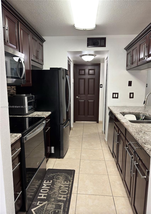 kitchen with light tile patterned floors, visible vents, appliances with stainless steel finishes, light stone countertops, and a sink