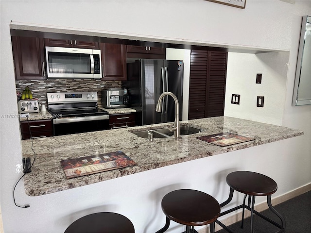 kitchen featuring light stone counters, stainless steel appliances, a sink, a kitchen breakfast bar, and decorative backsplash