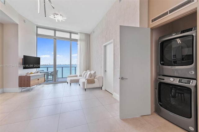 clothes washing area featuring light tile patterned floors, stacked washer and dryer, laundry area, and baseboards