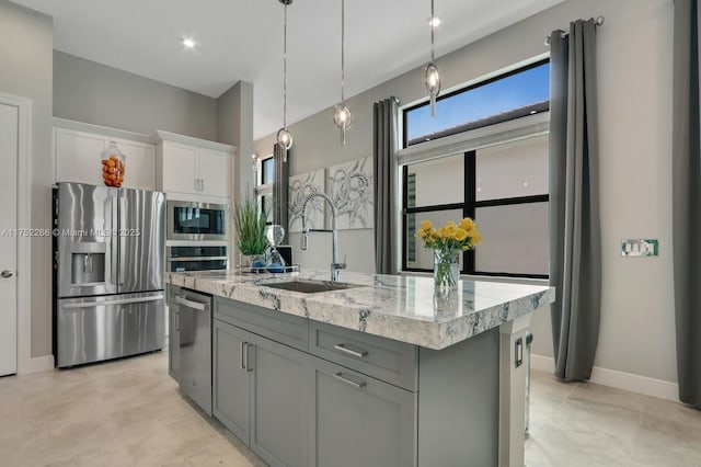 kitchen featuring light stone counters, a sink, white cabinetry, appliances with stainless steel finishes, and decorative light fixtures