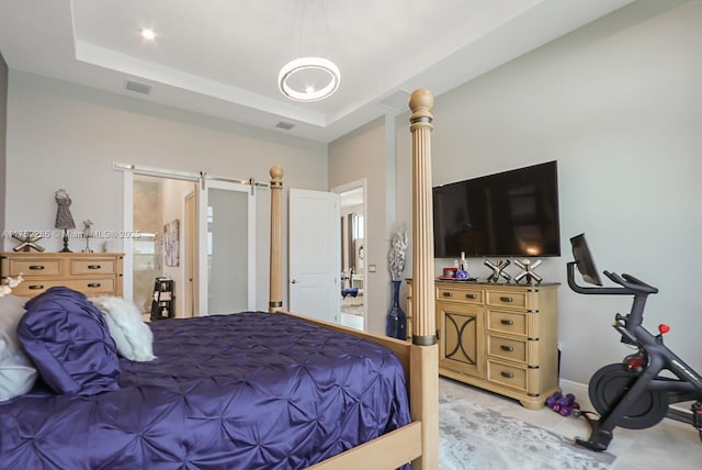 bedroom with a raised ceiling, visible vents, ornate columns, and a barn door