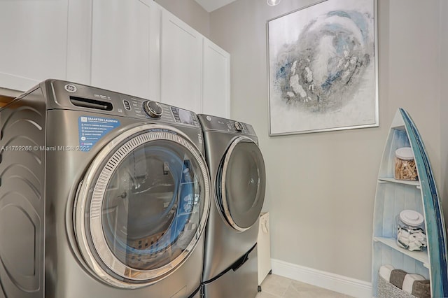 washroom with light tile patterned floors, washer and clothes dryer, cabinet space, and baseboards