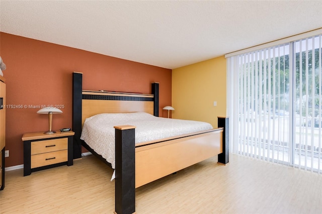 bedroom with light wood-style floors, access to exterior, and a wall of windows