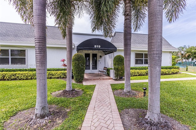 view of front facade with french doors, a front yard, a shingled roof, and stucco siding