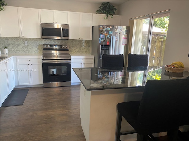 kitchen featuring tasteful backsplash, a breakfast bar area, dark wood-type flooring, stainless steel appliances, and white cabinetry