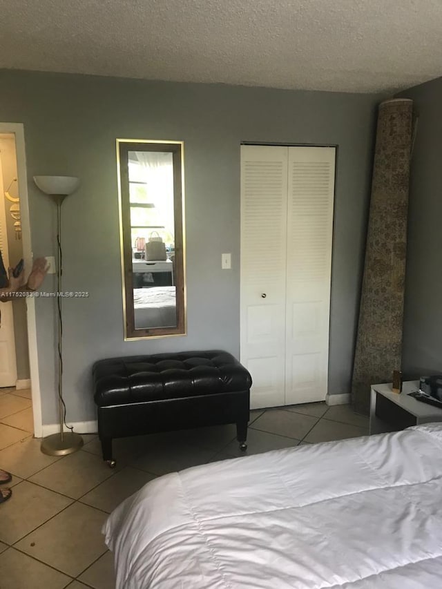 tiled bedroom featuring a closet, a textured ceiling, and baseboards