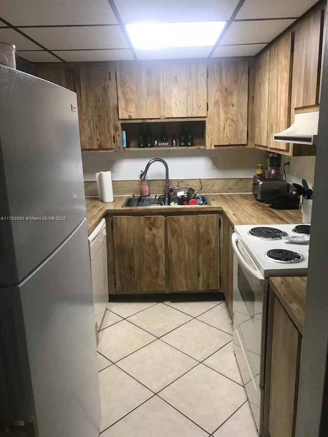 kitchen with white appliances, light tile patterned floors, wood counters, under cabinet range hood, and a sink