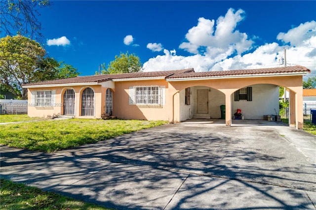 mediterranean / spanish-style house featuring aphalt driveway, a front yard, a carport, and stucco siding