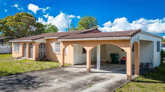 view of front facade featuring an attached carport, a tile roof, driveway, stucco siding, and a front yard