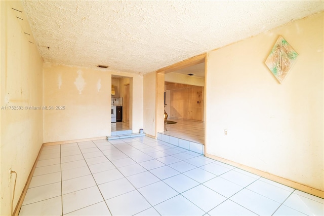 unfurnished room with a textured ceiling, baseboards, visible vents, and tile patterned floors