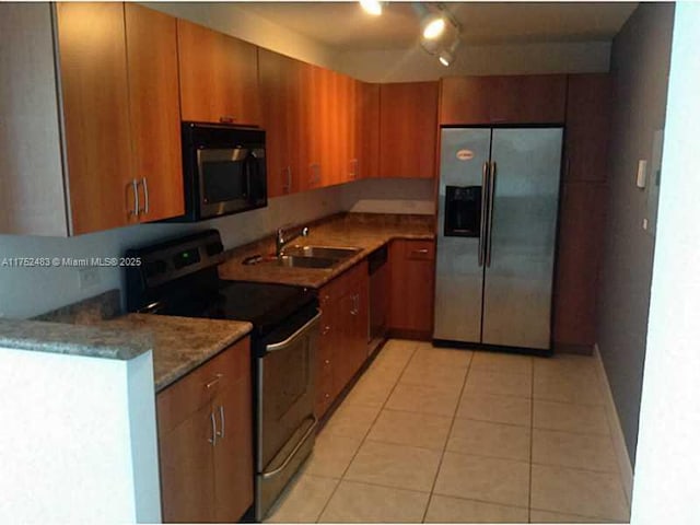 kitchen featuring appliances with stainless steel finishes, brown cabinetry, a sink, and light tile patterned floors