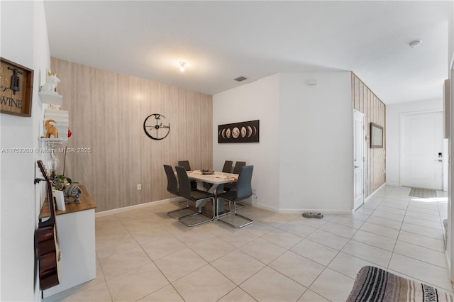 dining space with light tile patterned floors, wood walls, visible vents, and baseboards