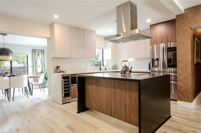 kitchen with modern cabinets, stainless steel fridge, white cabinetry, and island range hood