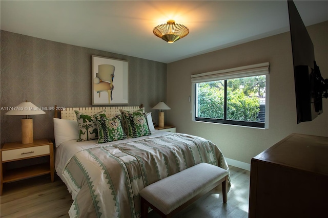 bedroom featuring wood finished floors, baseboards, and wallpapered walls