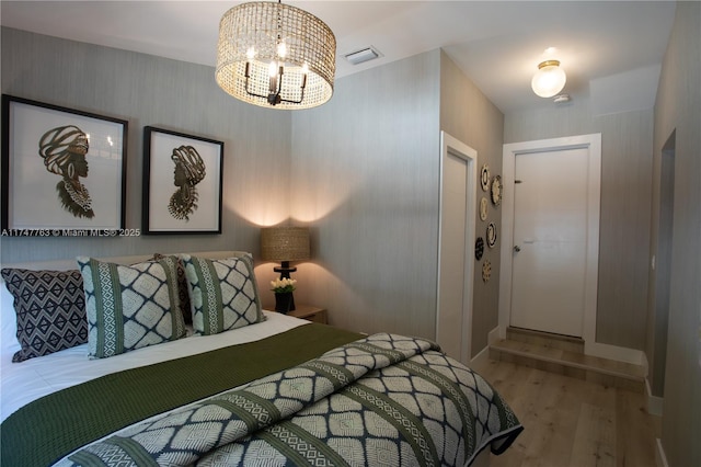 bedroom with visible vents, wood finished floors, a chandelier, baseboards, and wallpapered walls