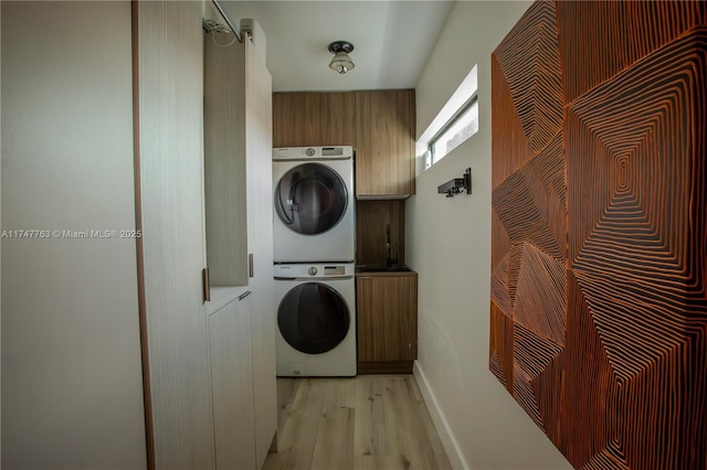 washroom featuring light wood-style floors, stacked washer / drying machine, cabinet space, and baseboards