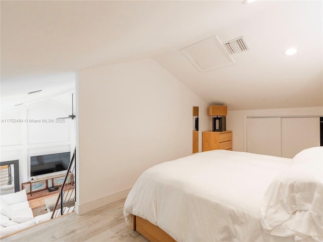 bedroom with attic access, visible vents, vaulted ceiling, and light wood finished floors