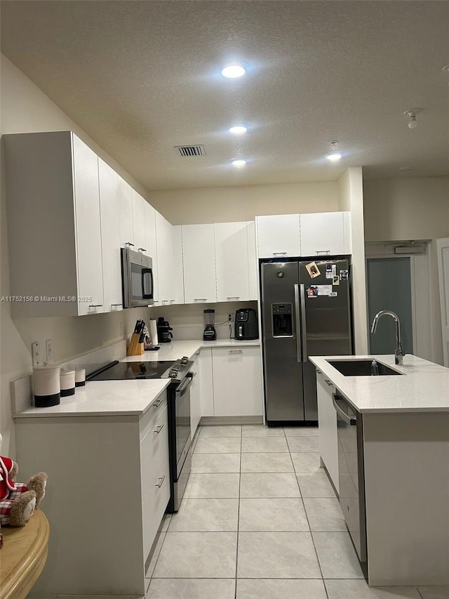 kitchen with light tile patterned floors, stainless steel appliances, light countertops, white cabinetry, and a sink