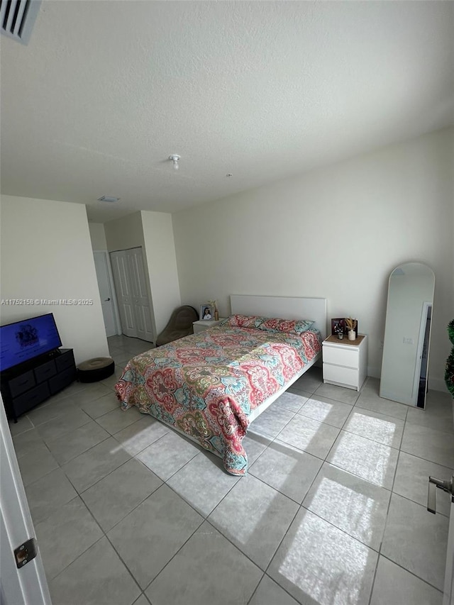 bedroom with visible vents, arched walkways, a textured ceiling, a closet, and light tile patterned flooring