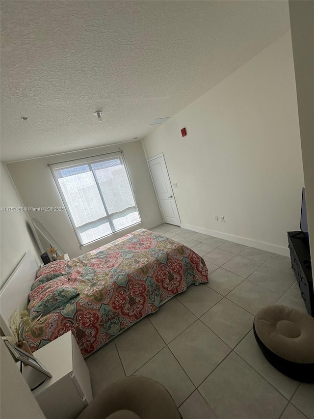 bedroom with light tile patterned floors, a textured ceiling, and baseboards