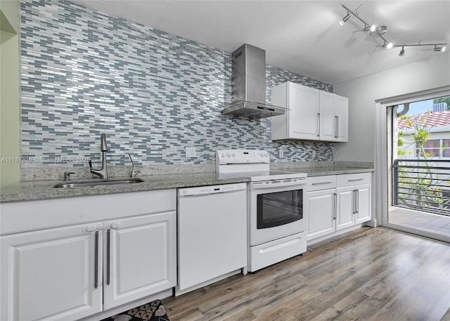 kitchen with white appliances, tasteful backsplash, white cabinets, wall chimney range hood, and a sink