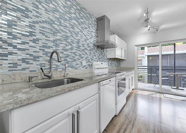 kitchen with light stone counters, white appliances, a sink, white cabinets, and wall chimney range hood