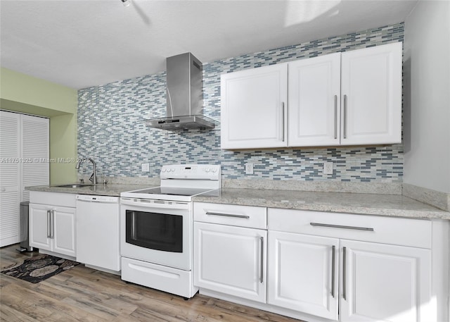 kitchen with white appliances, a sink, white cabinetry, decorative backsplash, and wall chimney exhaust hood