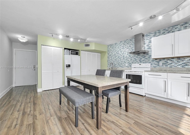 kitchen featuring white appliances, light wood finished floors, visible vents, wall chimney range hood, and white cabinetry