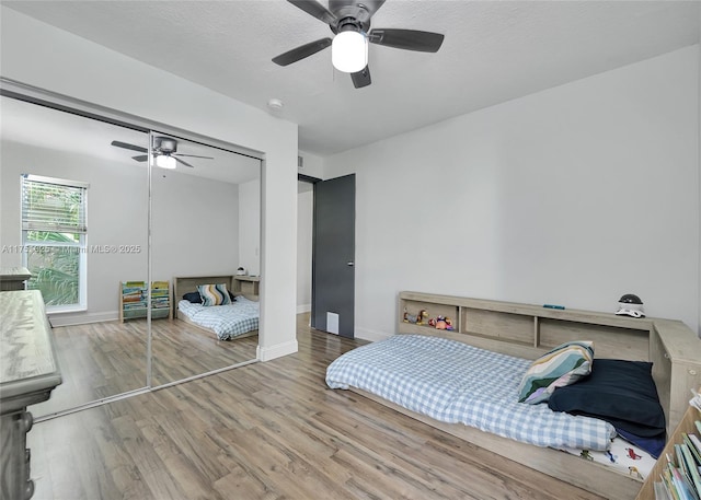 bedroom with a closet, a ceiling fan, a textured ceiling, wood finished floors, and baseboards