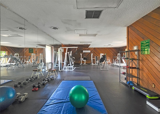 workout area with attic access, visible vents, a textured ceiling, and wooden walls